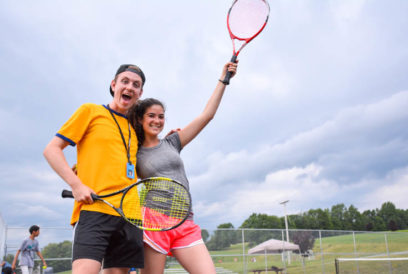 Two campers with tennis rackets on the tennis court