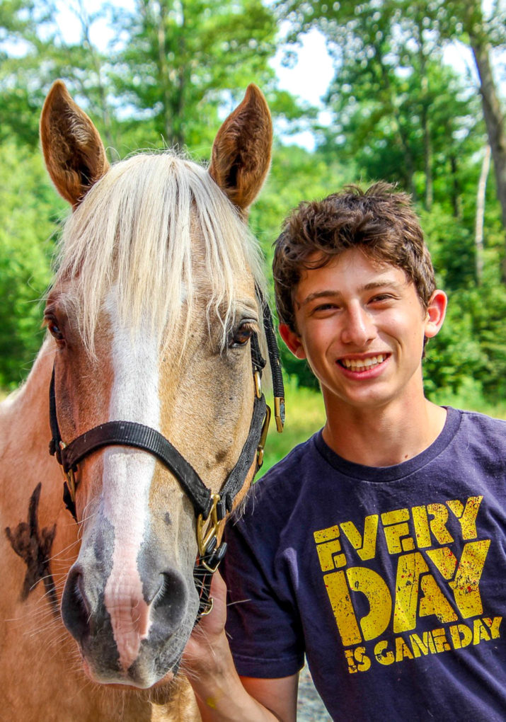 Boy camper smiling next to a horse