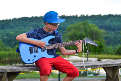 Boy camper playing the electric guitar outside