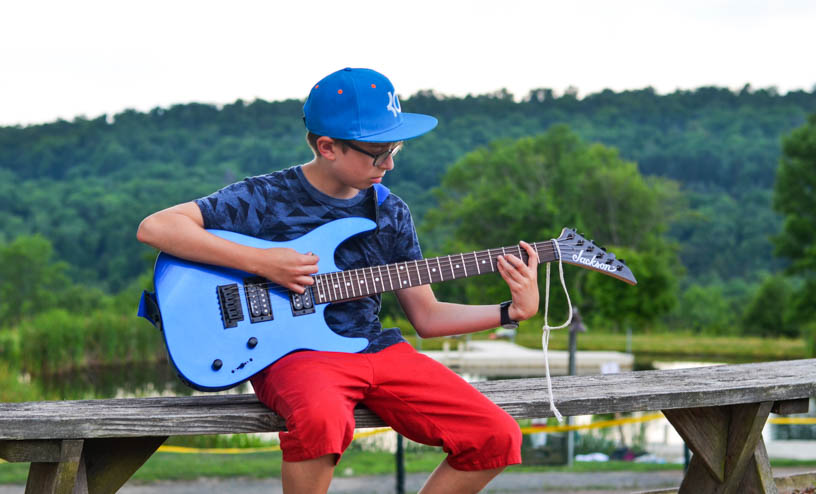 Boy camper playing the electric guitar outside