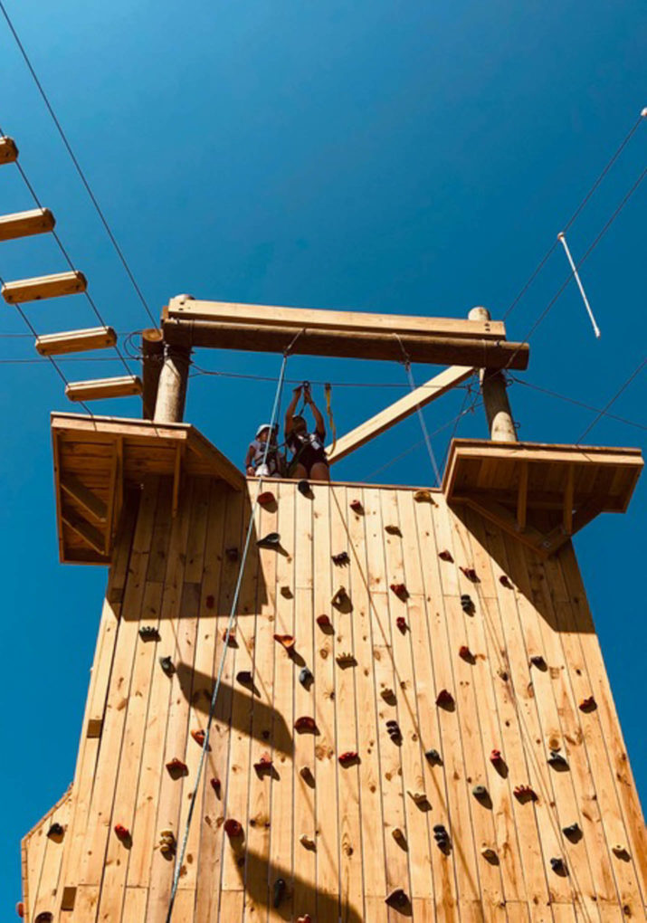 Camper at the top of the rock wall on the challenge course