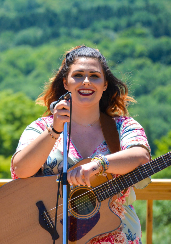 Girl camper singing and playing guitar on stage outside