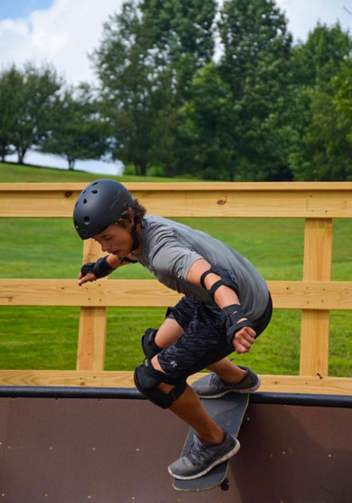 Camper about to skateboard down a half pipe ramp