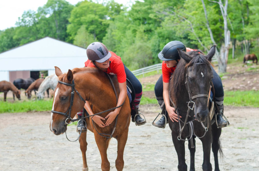 Two campers on horses bending over hugging their horses necks