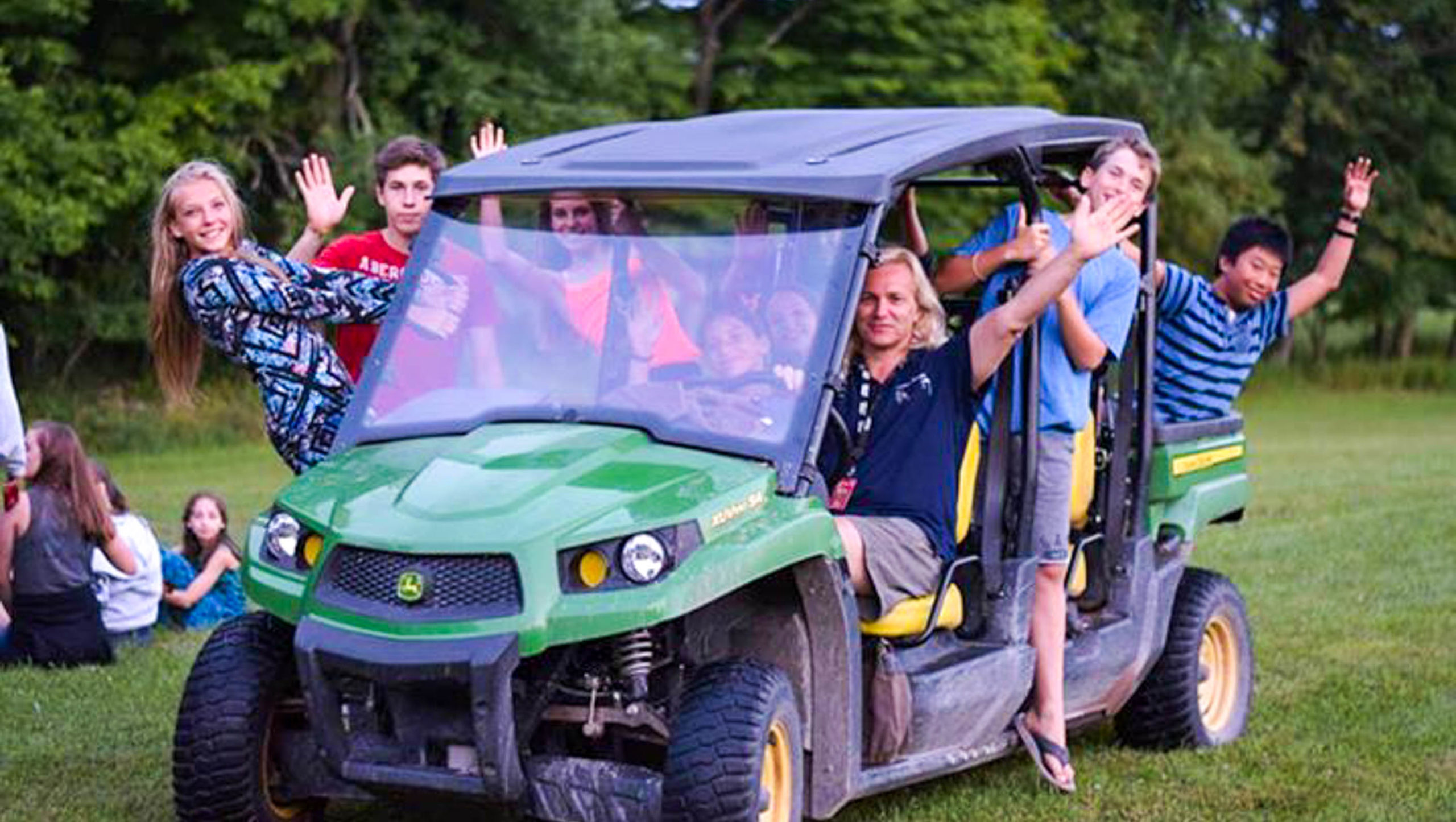 Director Nigel driving a golf cart with a bunch of campers