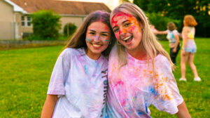 Two female campers covered in powder paint from taking part in a summer camp color run at a teen summer camp.