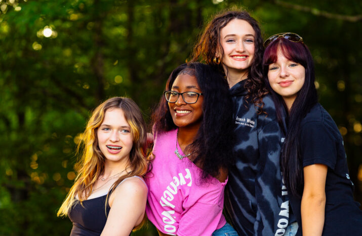 A group of teen girls posing as the sun sets on a summer camp camp fire