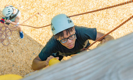A teen boy climbing the high ropes course at summer camp
