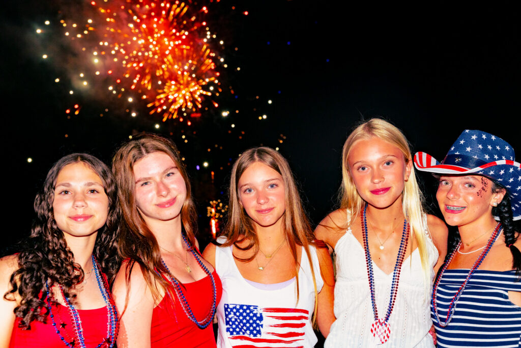 A group of teen girls posing in front of a fireworks display on the 4th of July at summer camp