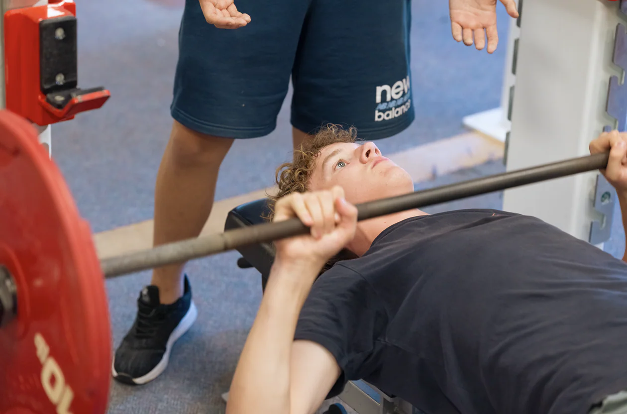 A teen camper bench pressing with supervision in the fitness center at New York Teen Camp